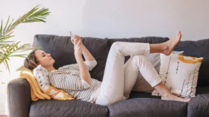 Uma mulher deitada no sofá com um celular na mão.
